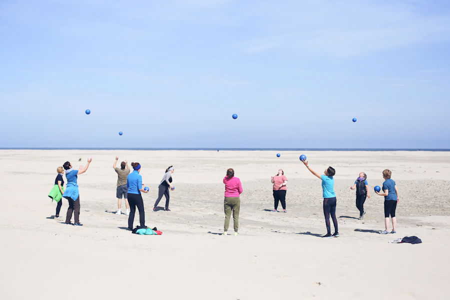 Eine Gruppe am Strand macht Bewegungsübungen mit Bällen